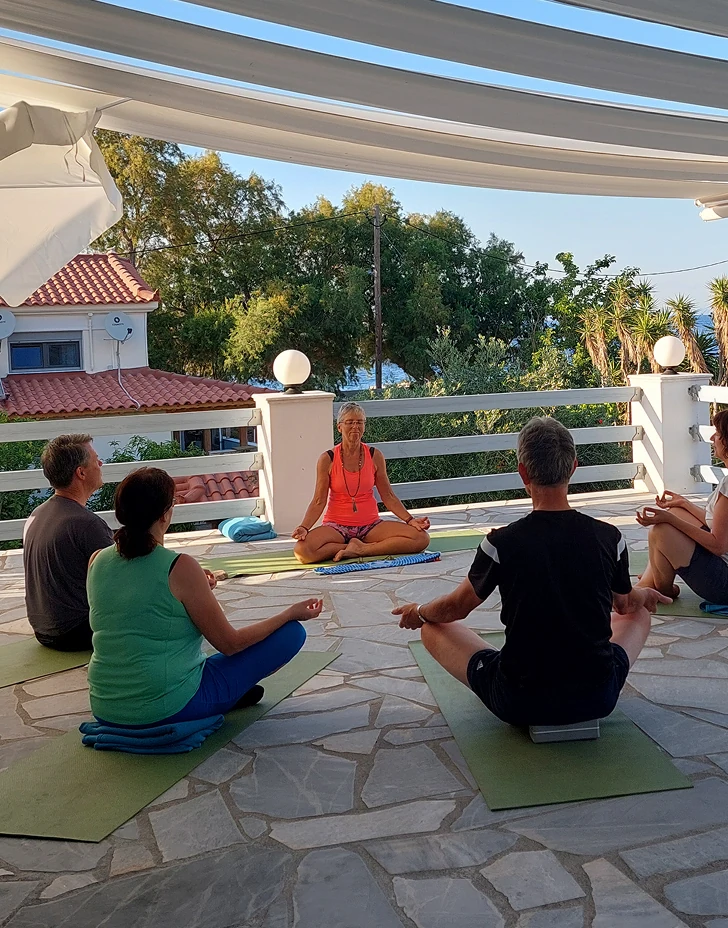 Een groep mensen volgt een begeleide mindfulness-sessie op yogamatten op een zonnig terras in Samos.