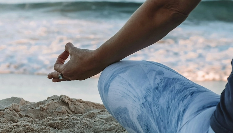Vrouw in meditatiehouding op het strand tijdens een mindfulnesssessie op Samos.