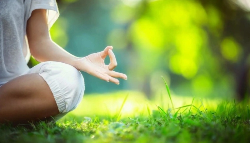 Persoon in meditatiehouding in het gras tijdens een online mindfulnesscursus van Marjaani.