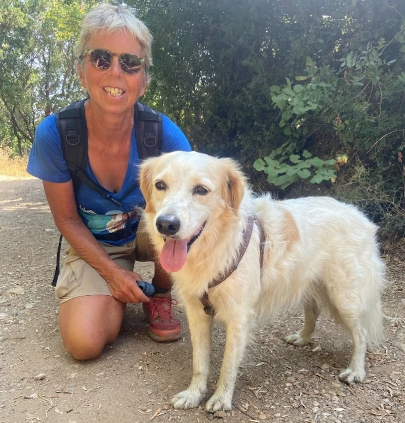 Vrouw wandelt met haar blije hond op een bosachtig pad.