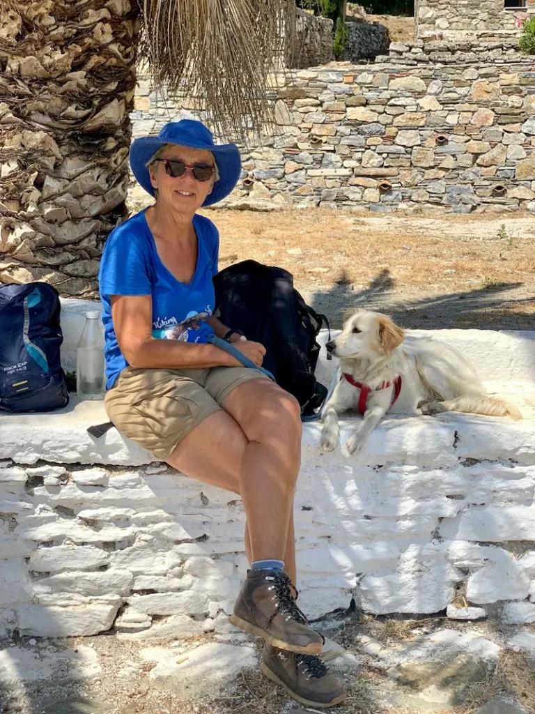 Vrouw genaamd Marjaani zit onder een palmboom op een stenen bank met een witte hond naast zich.