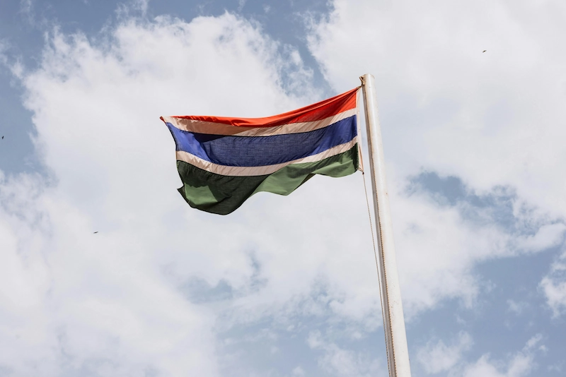 De nationale vlag van Gambia wappert aan een vlaggenmast tegen een bewolkte lucht.