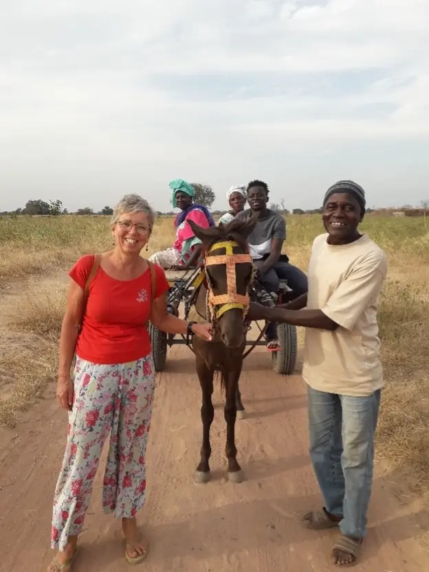 Marjaani en een man poseren naast een ezel met een kar, waarop drie mensen zitten, op een zandweg in Gambia.