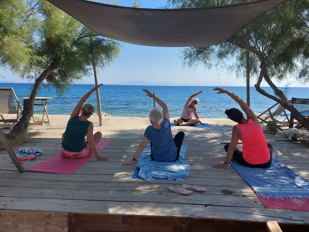 Groepsyogales op een houten vlonder aan zee onder schaduwdoeken bij Marjaani Yoga.